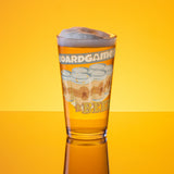 16-ounce glass pint glass printed with "Boardgames & Beer" text above an illustration of a six-pack of beer cans.