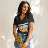 A woman wearing a black graphic t-shirt with a 'Boardgames' theme, paired with light blue jeans, holding a small bouquet of yellow flowers against a warm, sunlit beige background.
