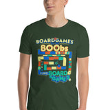 A man wearing a dark green graphic t-shirt with a colorful board game design that reads 'BOARDGAMES ARE LIKE BOOBS I LIKE BOARD GAMES'.