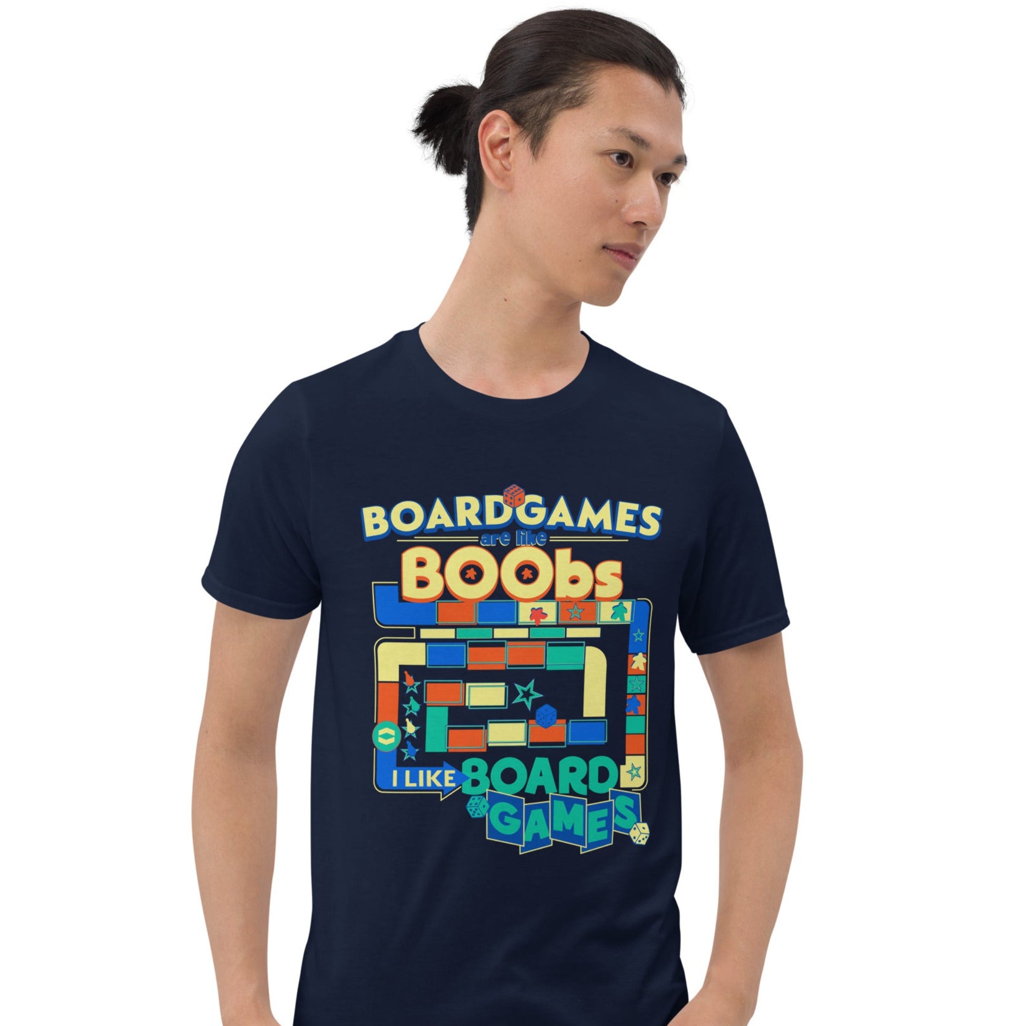 A man wearing a navy blue t-shirt with a colorful retro-style board game graphic and text that reads 'BOARDGAMES ARE LIKE BOOBS I LIKE BOARDGAMES'.