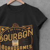 A black short-sleeve t-shirt on a wooden hanger against a textured gray wall. The shirt features a large vintage-style graphic in gold and orange reading 'Bourbon & Boardgames' with 'Sip & Play' and 'The Day Away' around a whiskey glass illustration.