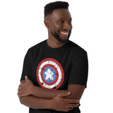 A smiling man wearing a black crewneck t-shirt with a distressed  shield graphic on the chest with a meeple at the center, against a plain white background.