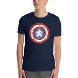 A man wearing a navy blue crewneck t-shirt with a distressed shield graphic on the chest with a meeple at the center, paired with gray jeans, against a plain white background.