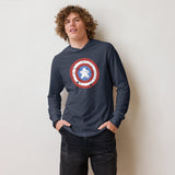 A young man with curly light brown hair wearing a navy blue long-sleeve hoodie with a Captain Meeple shield graphic on the chest, paired with black denim shorts, standing against a plain off-white wall.