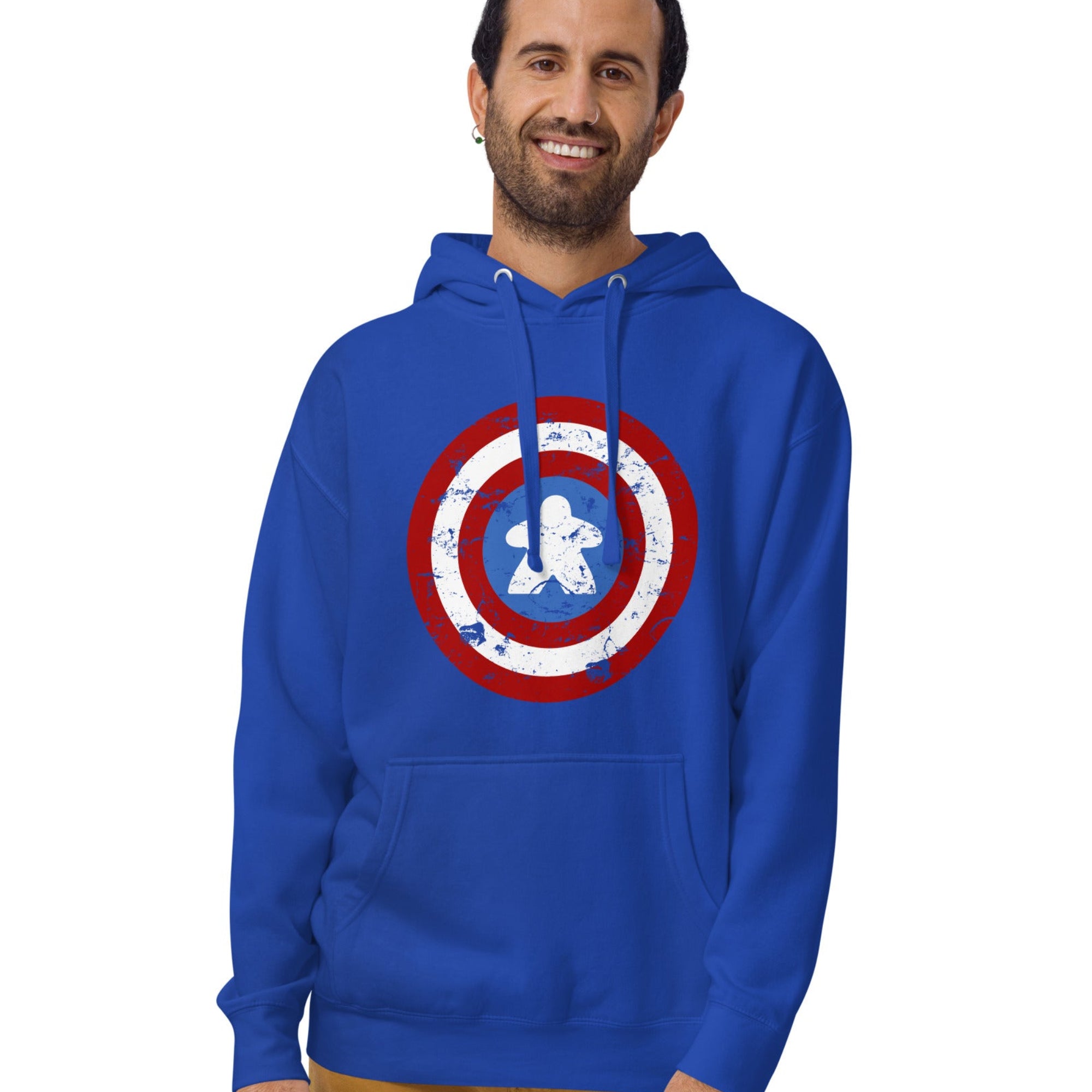 A man wearing a royal blue hoodie with a distressed Captain Meeple shield graphic on the chest, paired with tan pants, against a plain white background.