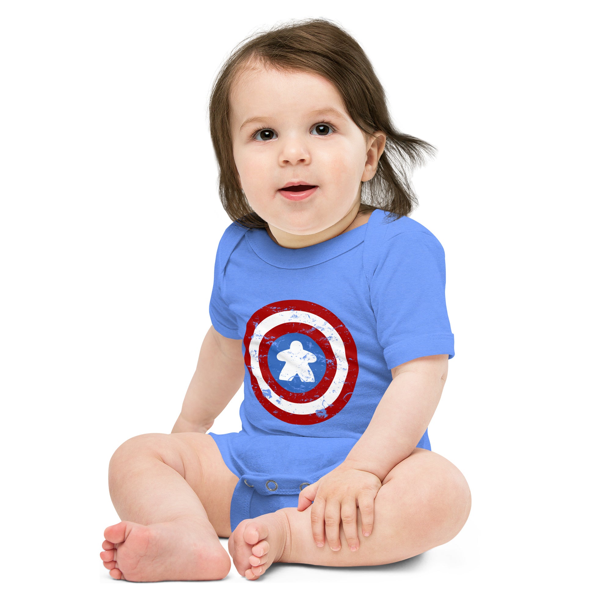 A baby sitting cross-legged wearing a blue short-sleeve bodysuit with a Captain meeple shield graphic on the front, photographed against a plain white background.