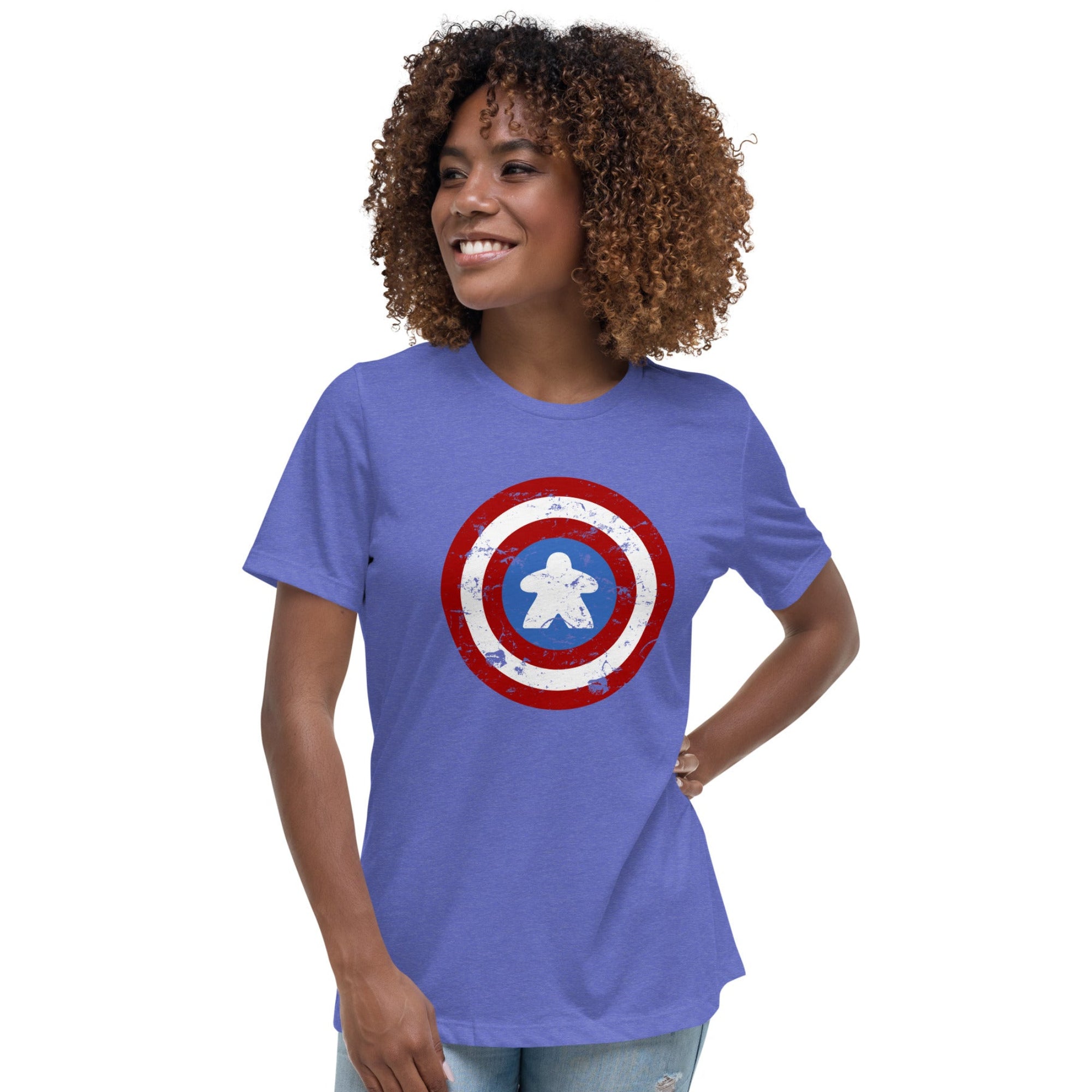 A woman with curly brown hair wearing a heathered periwinkle blue t-shirt with a distressed Captain shield graphic on the chest with a meeple in the center, paired with light wash jeans, against a plain white background.
