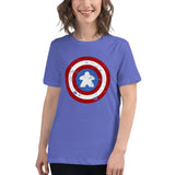 A woman wearing a short-sleeve crewneck t-shirt in periwinkle blue, featuring a distressed Captain  shield graphic on the chest with a meeple in the center. The background is a clean white studio backdrop.