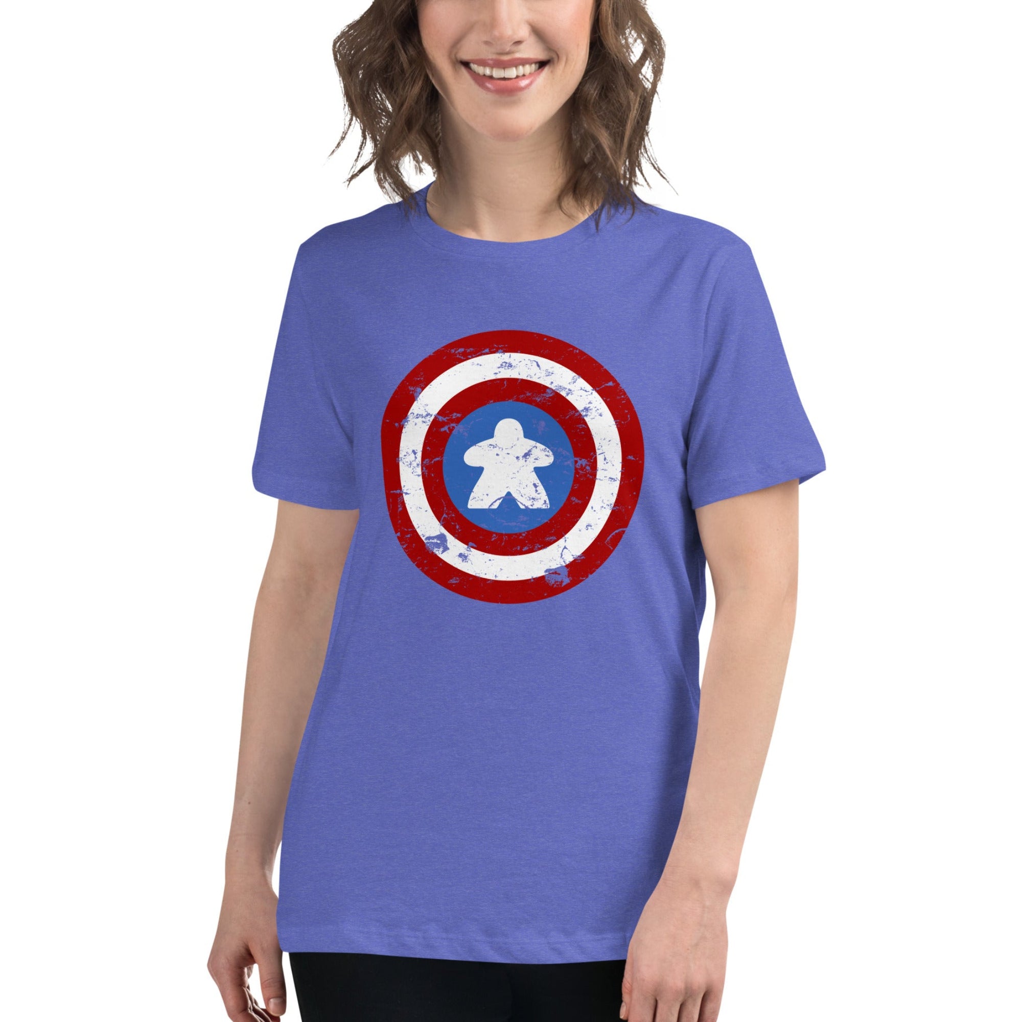 A woman wearing a short-sleeve crewneck t-shirt in periwinkle blue, featuring a distressed Captain  shield graphic on the chest with a meeple in the center. The background is a clean white studio backdrop.