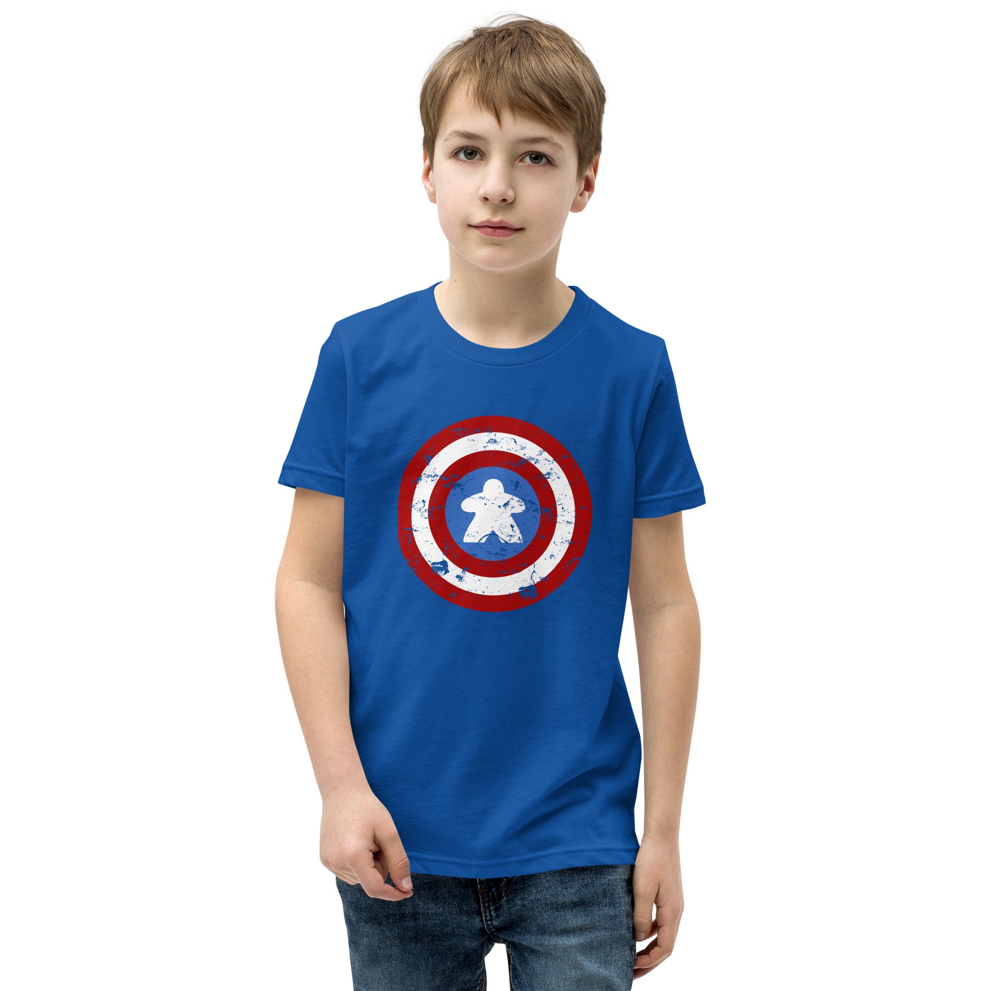 A young boy wearing a royal blue t-shirt with a Captain Meeple shield graphic on the chest, paired with dark wash jeans, standing against a plain white background.