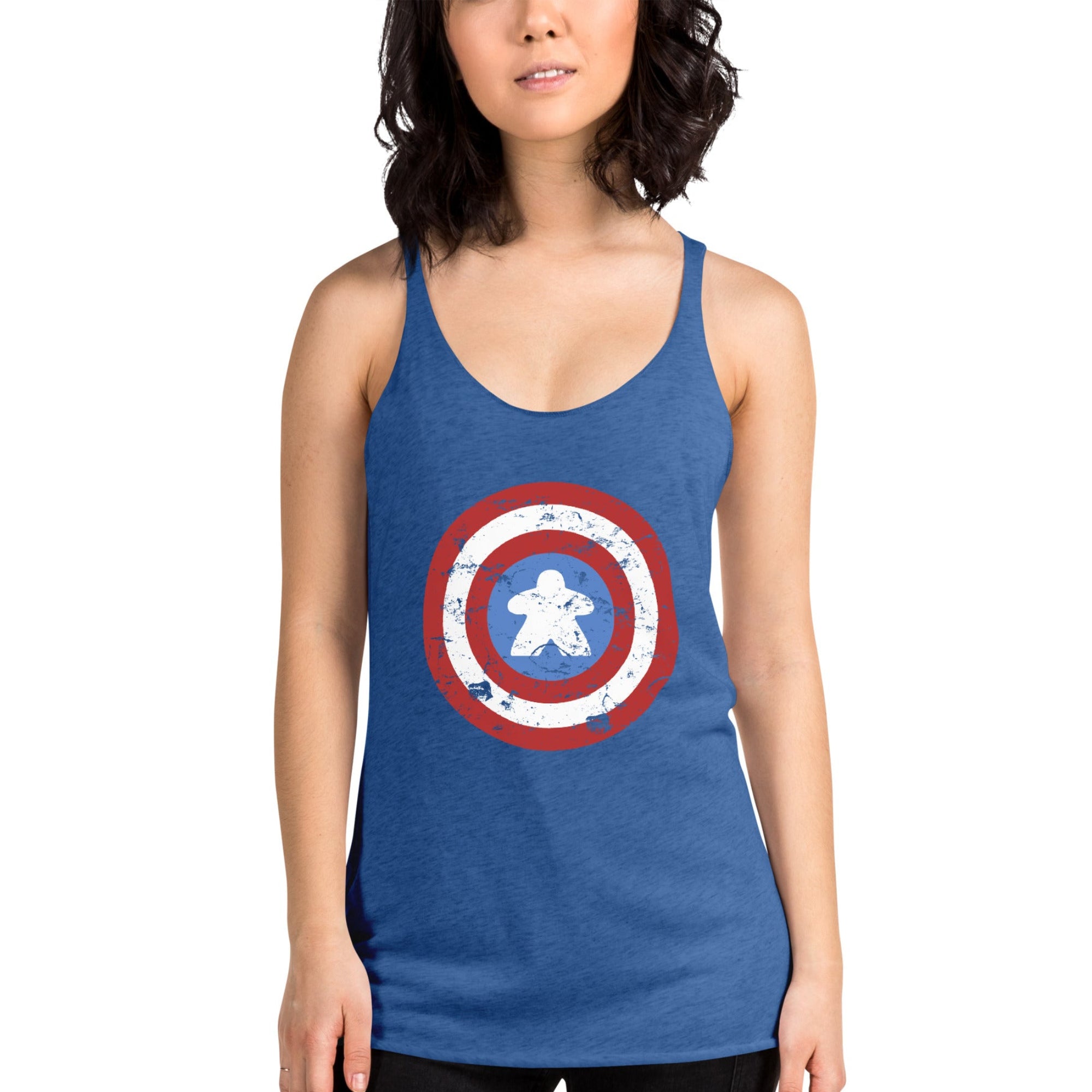 A woman wearing a heather blue racerback tank top with a distressed Captain Meeple shield graphic on the front with a meeple at the center instead of a star, paired with black pants, against a plain white background.