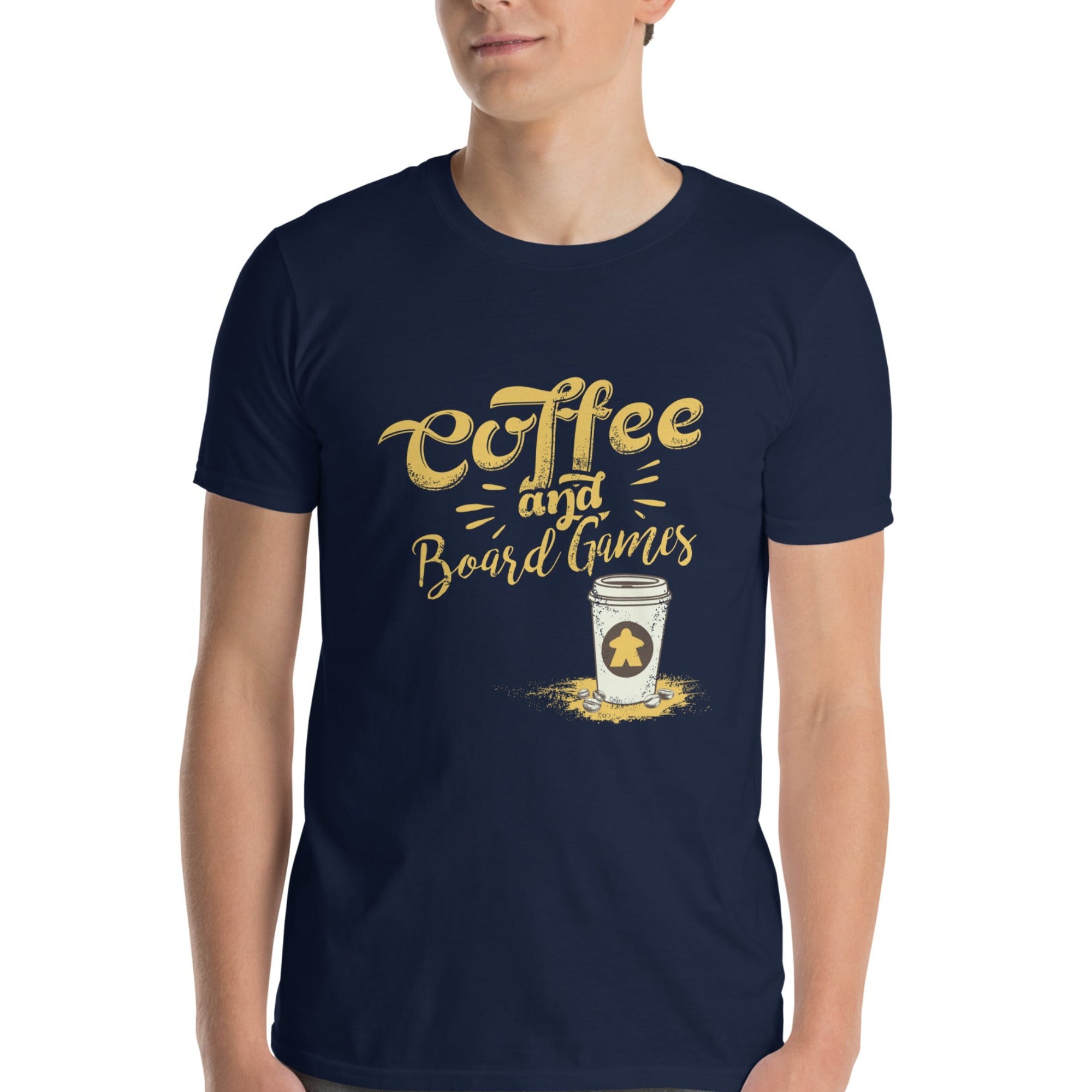 A man wearing a navy blue t-shirt with a gold and white graphic that reads 'Coffee and Board Games' with a cup illustration that has a meeple on it, paired with gray jeans, against a plain white background.