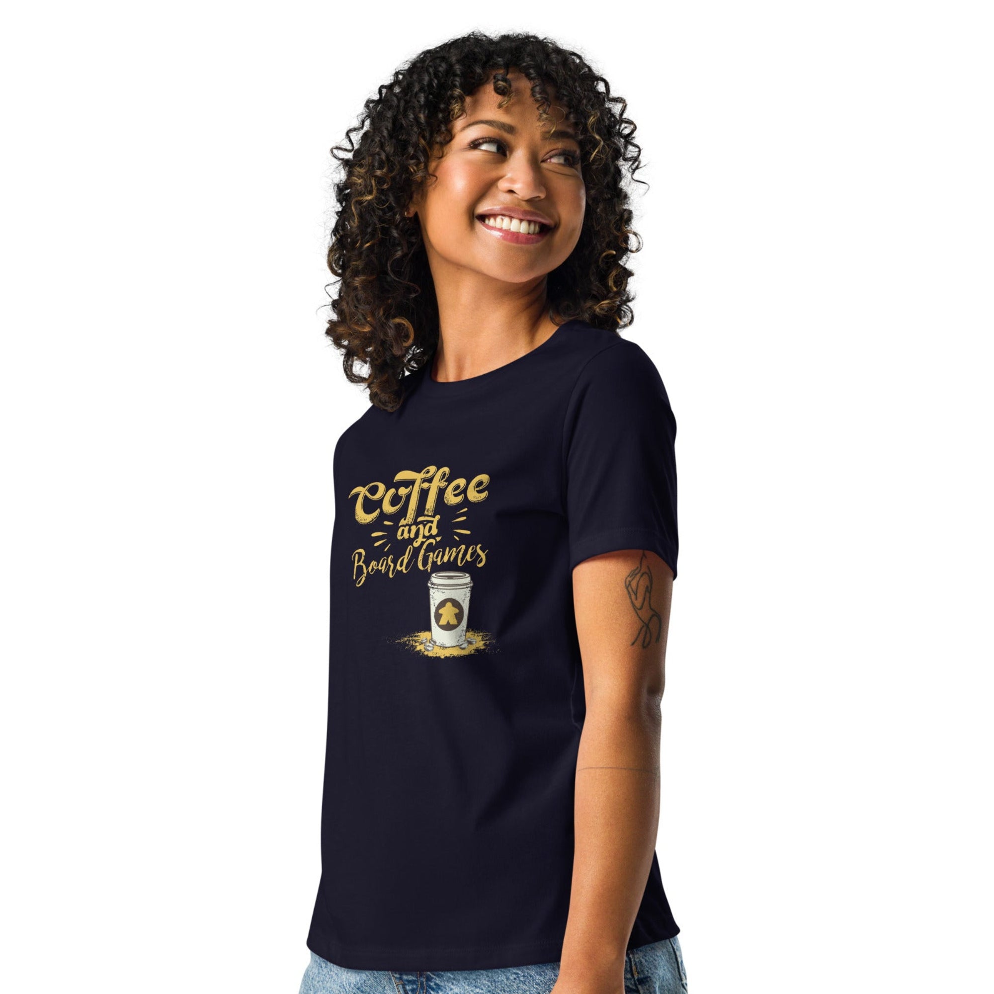 Woman wearing a navy blue t-shirt with the words Coffee and Board Games on the front and to go cup with a meeple on it