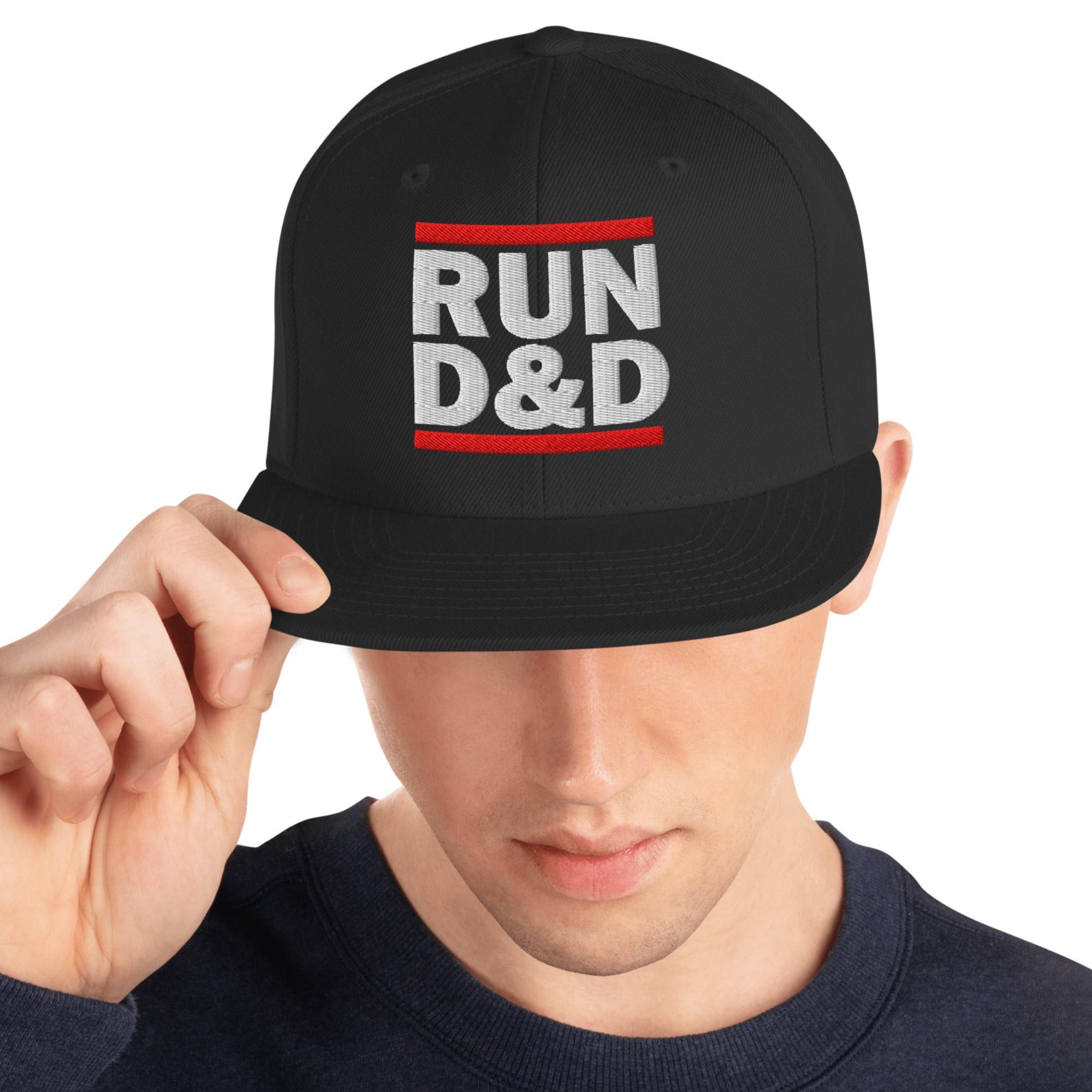 Man with head down wearing a black t-shirt and a black flat bill snapback hat with Run D&D embroidered on the front of it