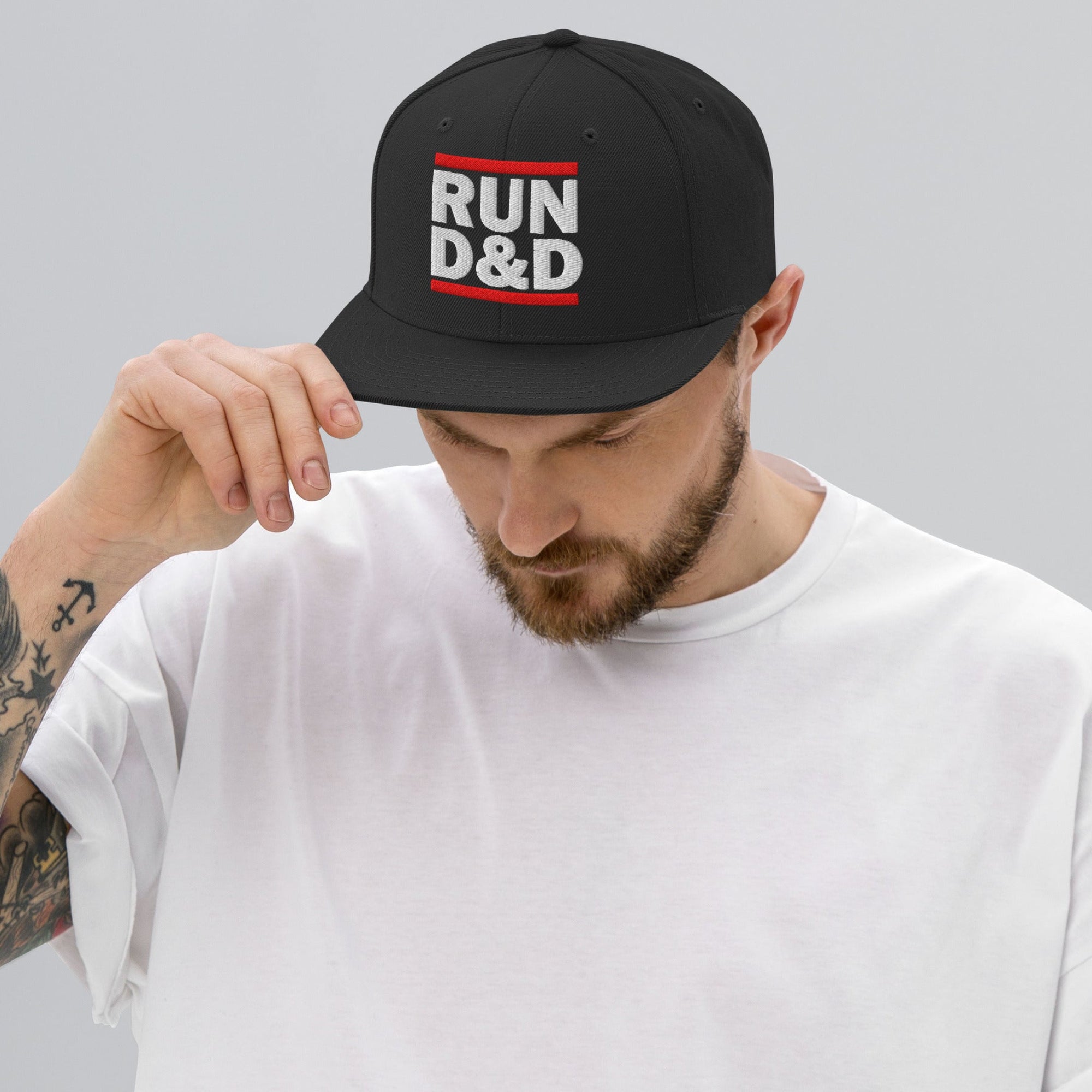 Man n white t-shirt wearing a black flat bill snapback hat with Run D&D Logo embroidered on the front
